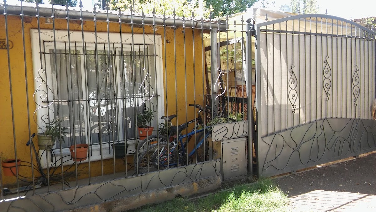 Fachada del taller de Herrería JLR en San Rafael: reja de ventana con volutas en hierro forjado y portón galvanizado sobre pared ocre.